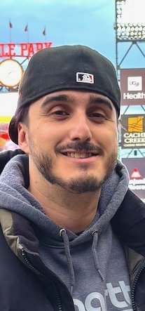 Smiling Latino man with baseball cap on backwards and facial hair