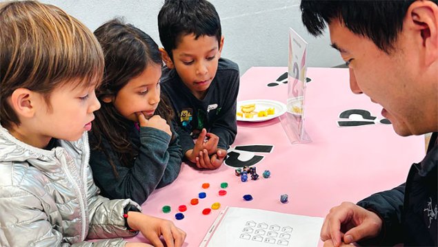 Three students play a math game with a parent volunteer.