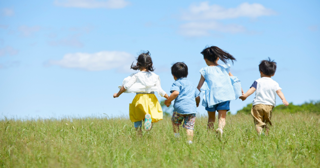 Four children holding hands running in a field. 