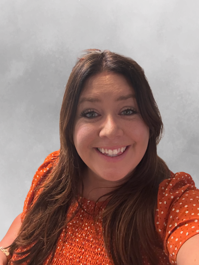 Woman with orange shirt and long straight brown hair smiles while looking at the camera
