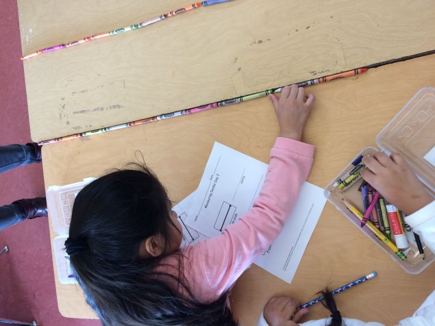 Girl using crayons to measure the length of a desk