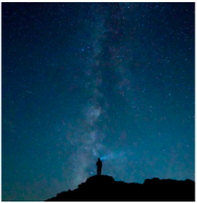 Person standing on a peak past twilight hours staring at the star filled night