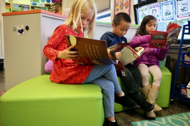 3 students sitting on a bench reading in their classroom. 