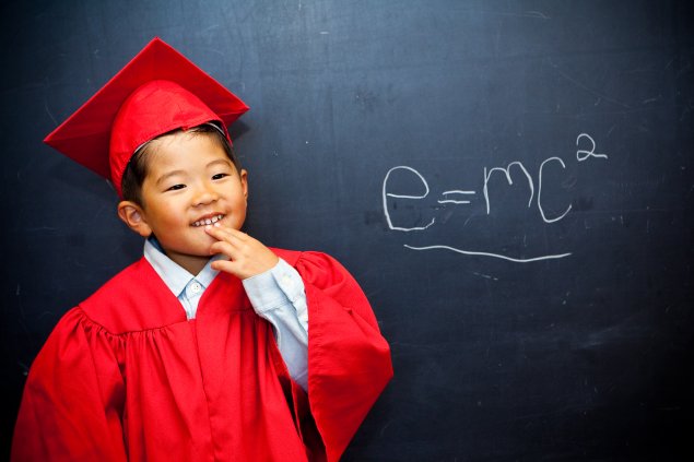 Elementary student in graduation robes by a chalkboard equation