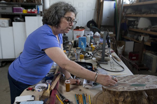 Image of a woman at a work table working on a large round wooden art piece ((Kevin N. Hume/S.F. Examiner)