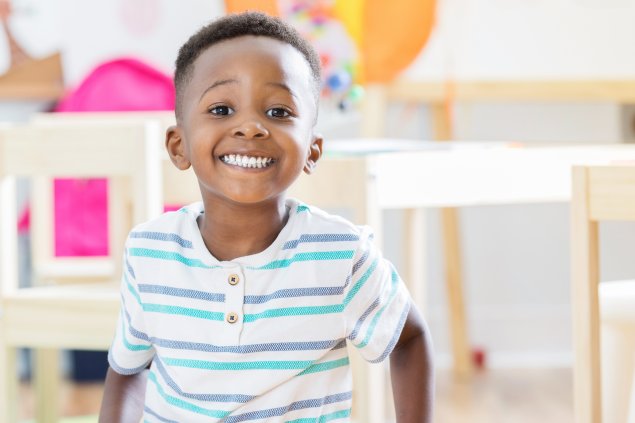 Preschool boy sitting on floor in his classroom and smiling at camera